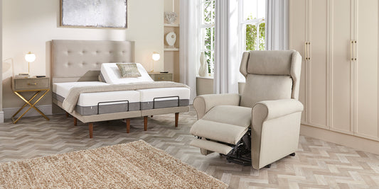 A riser recliner chair with the legrest extended with an adjustable bed in the background
