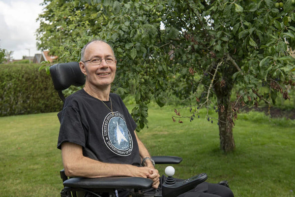 Older man sitting in a motorised wheelchair outside next to a tree
