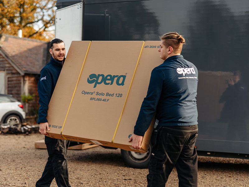 Two Opera delivery men carrying a cardboard box with Opera logo on it.