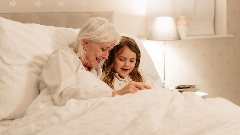 An older lady and her granddaughter are enjoying reading a book together in a Opera profiling bed
