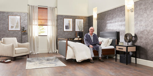 An older gentleman sat in a profiling care bed holding the wired handset