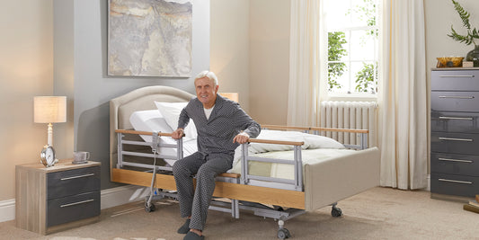 Elderly gentleman sitting on the edge of a profiling care bed with side rails up either side and his hands on them