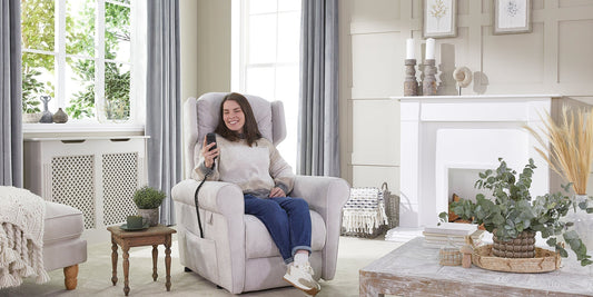 A woman with brown hair smiling sitting in a riser recliner chair holding the wired hand control and smiling
