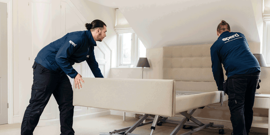 A profiling bed being installed in a bedroom by two gentleman wearing Opera branded jackets