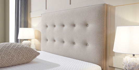 A linen coloured button headboard with a beige scatter cushion on top of the bed