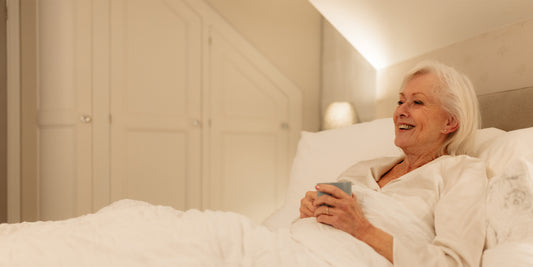 A older woman sat in bed smiling with a cup of tea