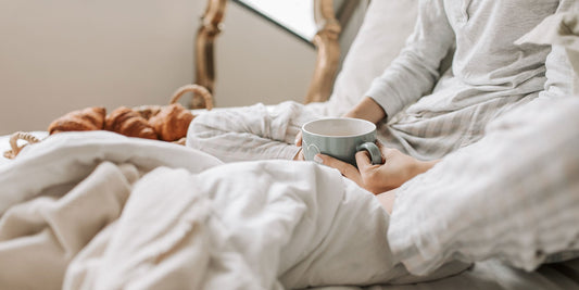 A person holding a cup of tea in bed with white bedsheets