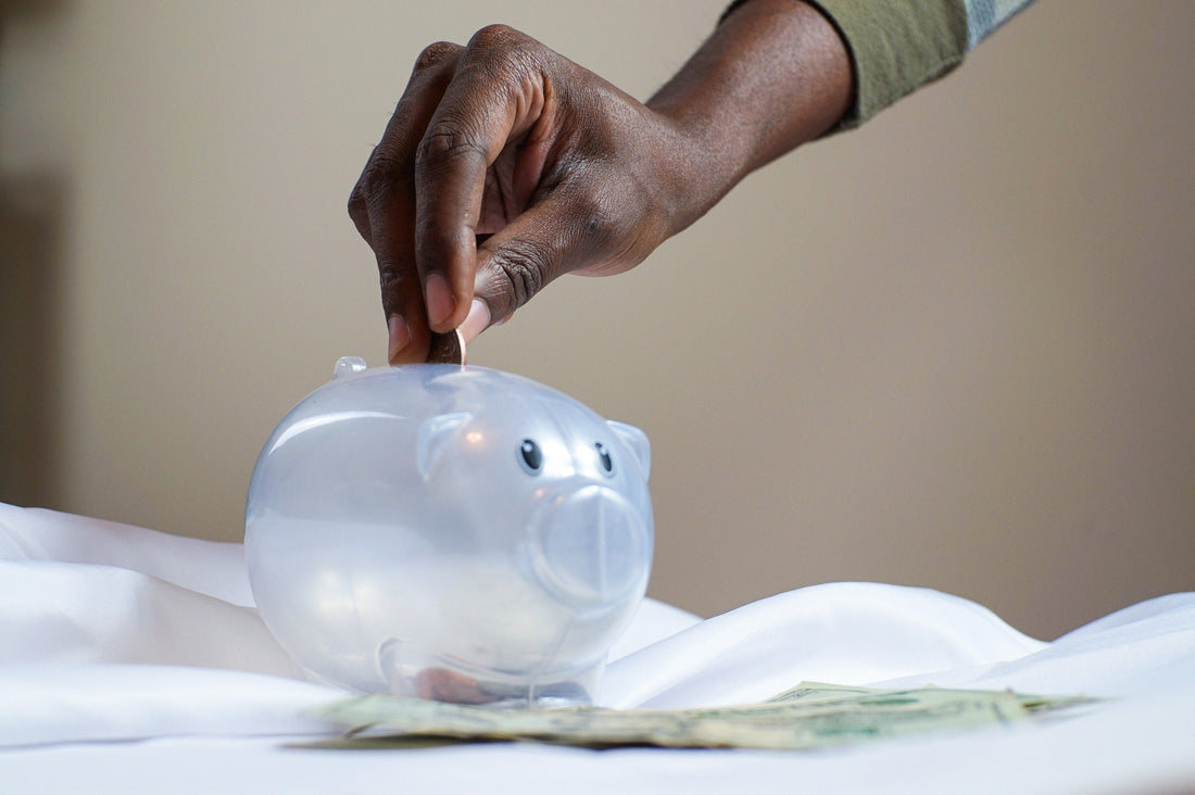 A clear piggy bank with a hand putting coins inside