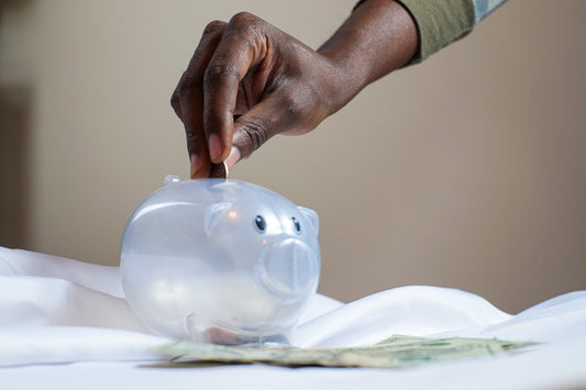 A clear piggy bank with a hand putting coins inside