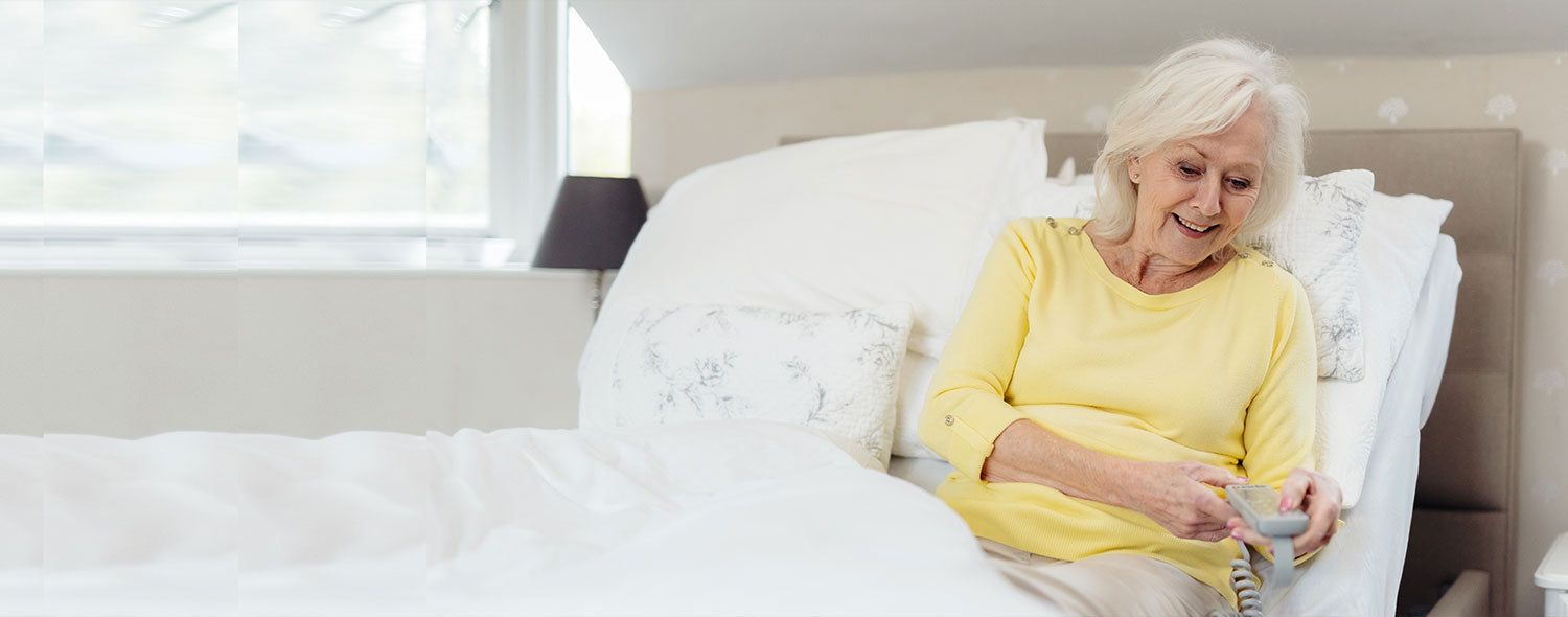 Older woman with a light yellow top using the remote control for her Opera profiling bed.