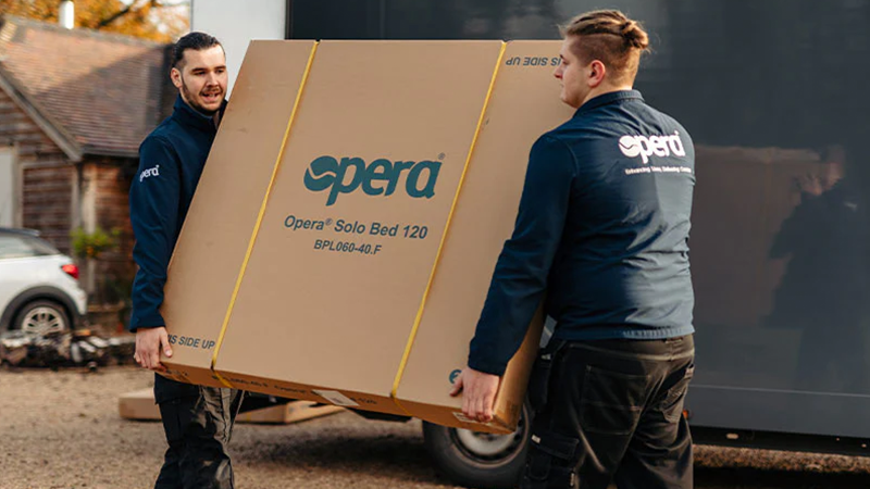 Two Opera installers carrying a large box containing the parts required to install an Opera solo bed.