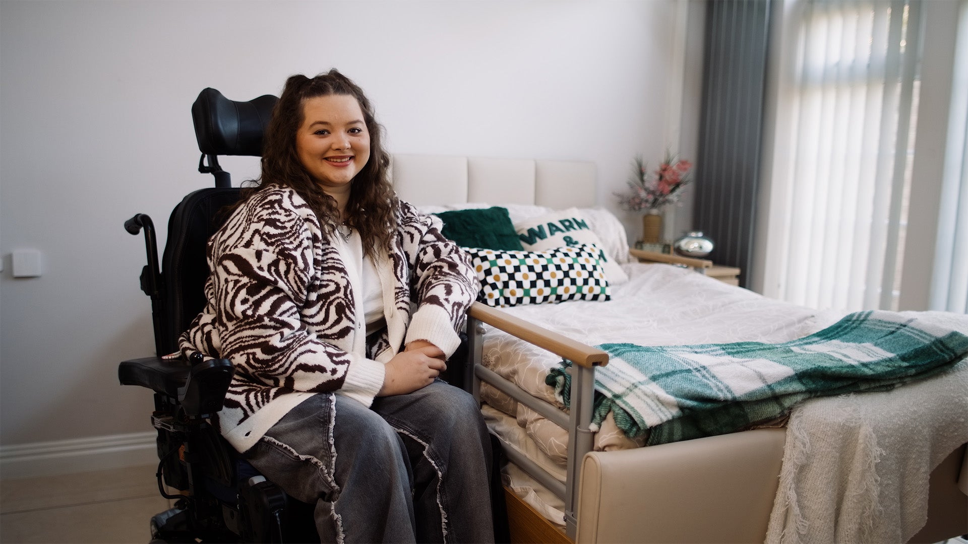 Opera Bed's customer Amy Pohl sitting in a wheelchair next to an Opera profiling bed