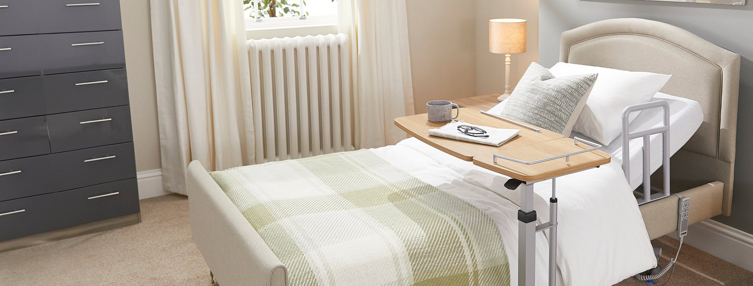 Opera hospital care bed with overbed table with a cup, notebook and pair of glasses on it.