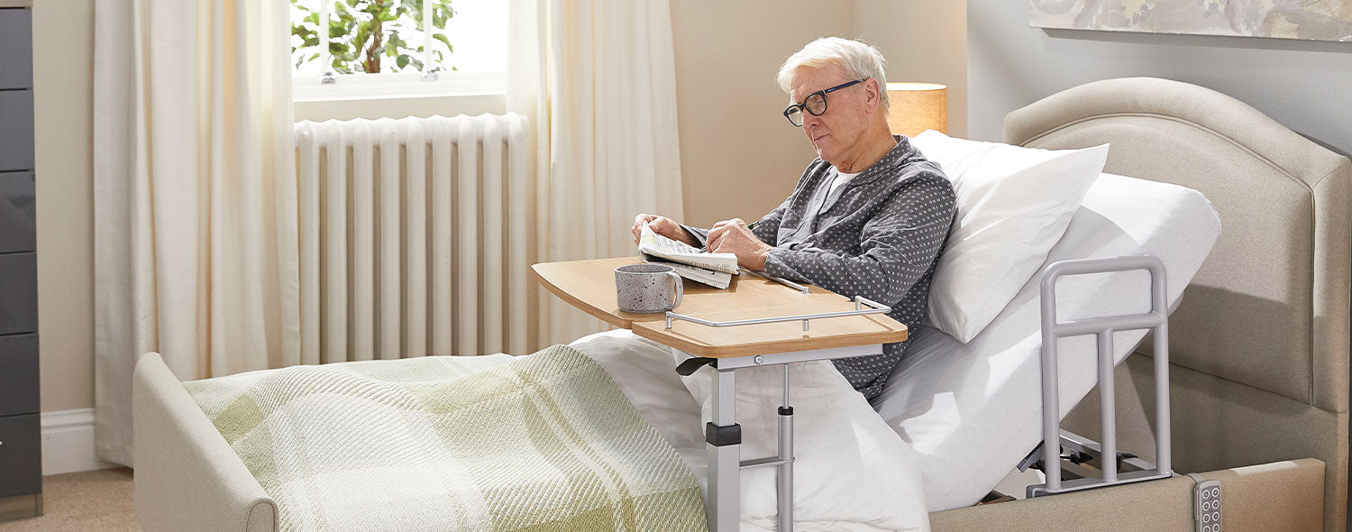 Older man reading a newspaper in an Opera profiling bed with a grab handle attached to the frame