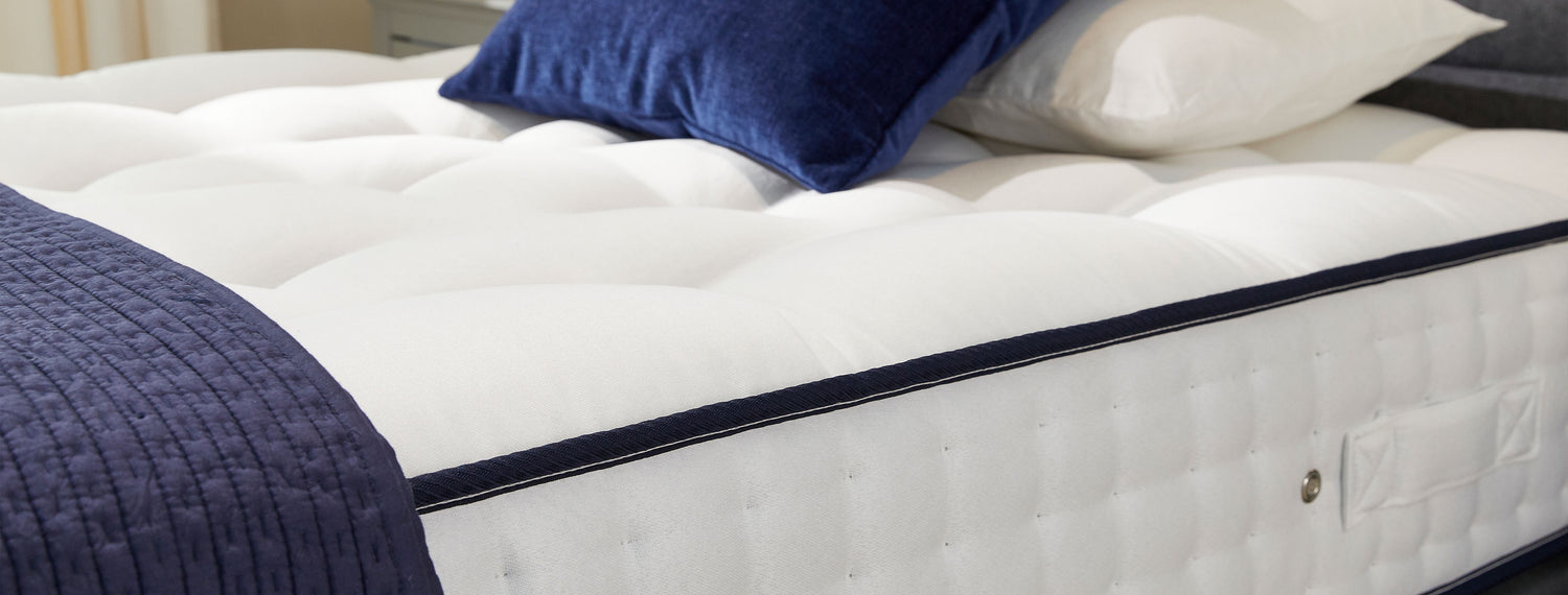 White Opera Beds comfort mattress with a navy blue sheet and pillow.