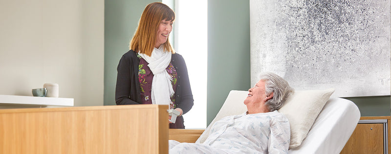 A carer adjusting the back rest of an older lady in a profiling bed
