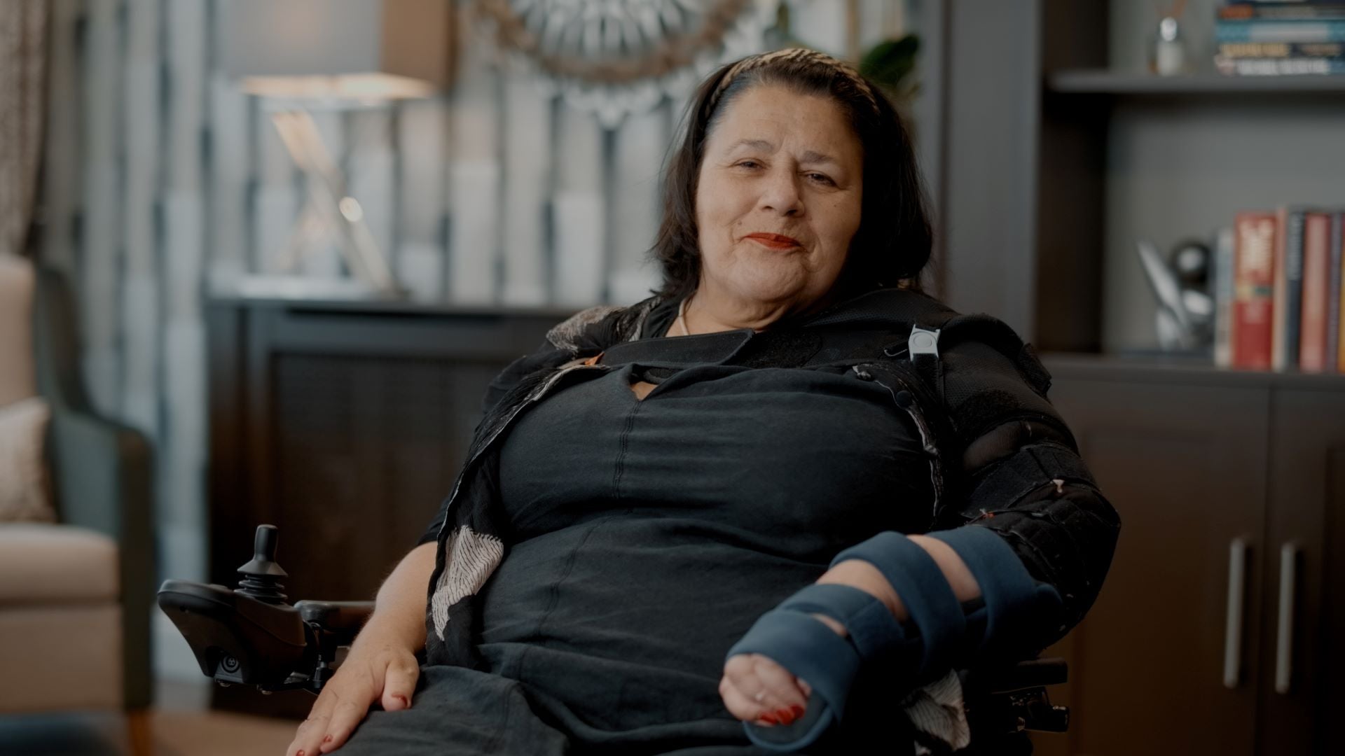 Liz wearing a black dress and sitting in a power assisted wheelchair