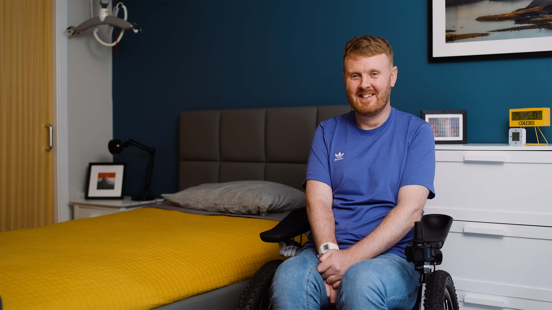 Opera Bed's customer Niall Harris sitting in a wheelchair next to an Opera profiling bed