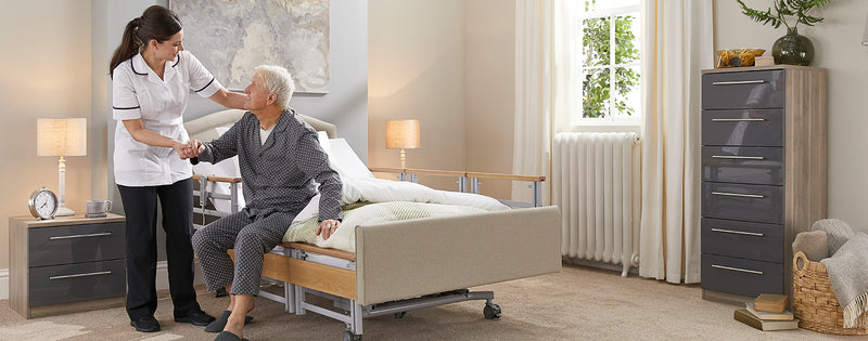A carer helping an older man get out of a profiling bed with side rails