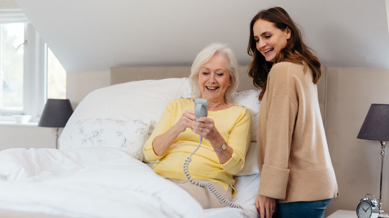 An older lady is showing her adult daughter how she controls her Opera profiling bed with a wired remote