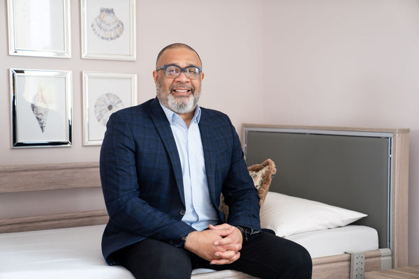 Billy, a man wearing a pale blue shirt and suit jacket sitting on the edge of an Opera Bed