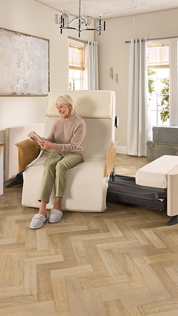 Lady sitting in a Rotating Chair Bed in the chair position, holding the remote control.